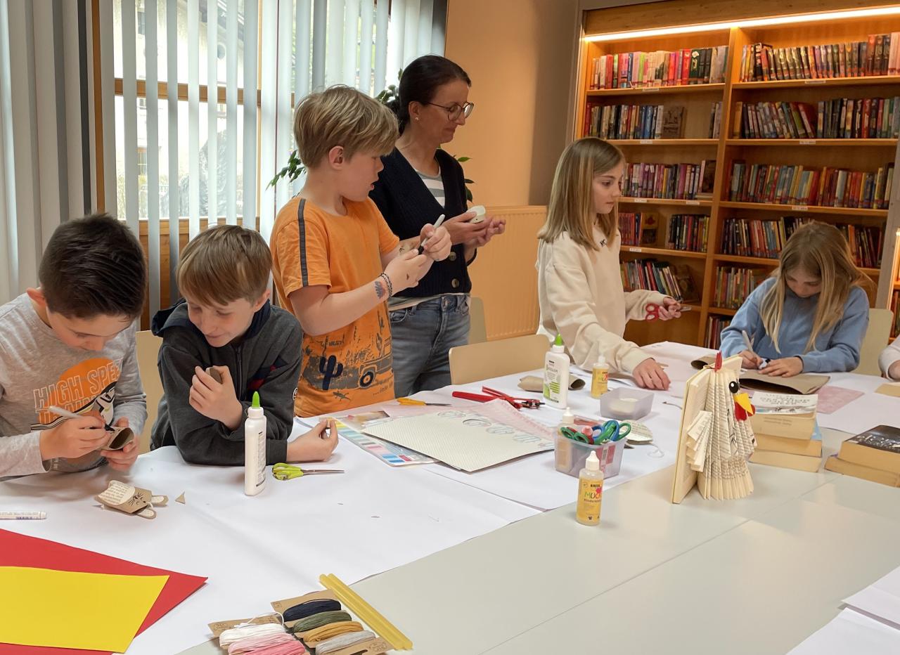 Kinder beim Osterbasteln am Tisch, dahinter Bücherregale